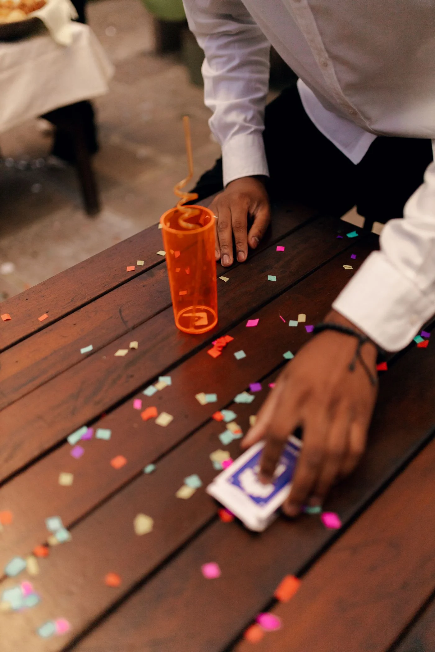 Person gathering colorful confetti from a wooden party table. — illustrative photograph.