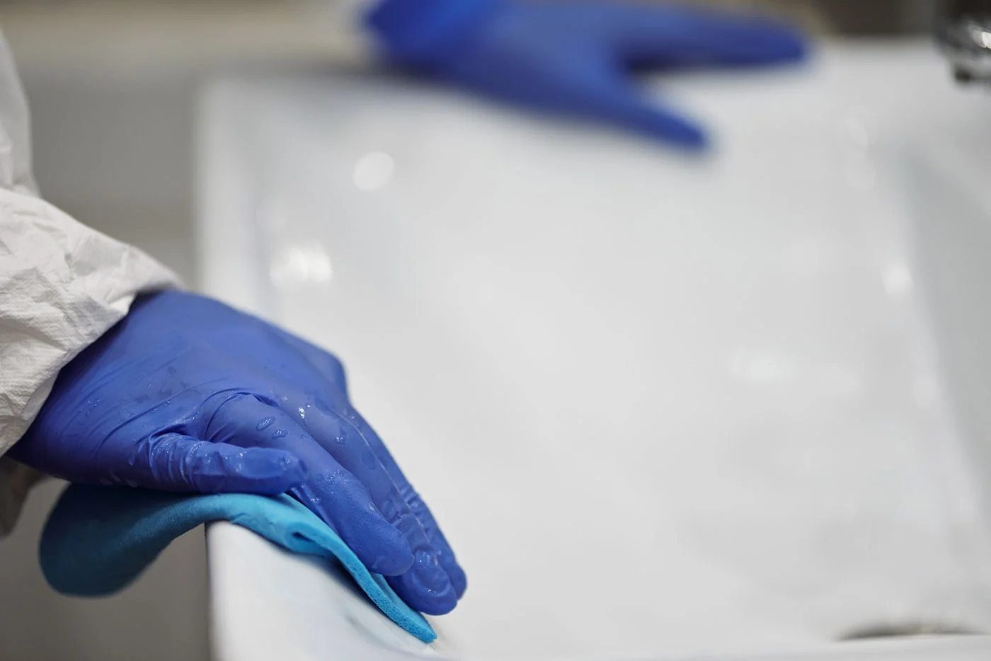 Blue-gloved hands cleaning a white bathroom sink. — illustrative photograph.